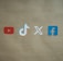 Four social media platform logos are arranged on a brown background. From left to right, the logos are for YouTube in red, TikTok in a combination of red, blue, and white, X in white, and Facebook in blue.